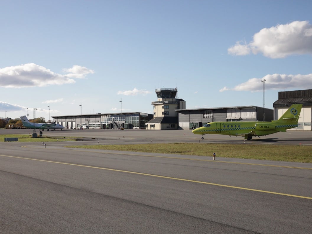 To fly på flyplassen i klart vær med flytårn og hangarer i bakgrunnen.