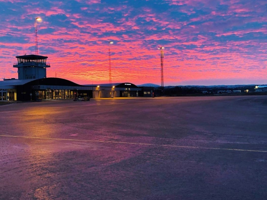 Lakselv flyplass ved solnedgang med fargerik himmel i rosa og blåtonar, terminalbygning og kontrolltårn.