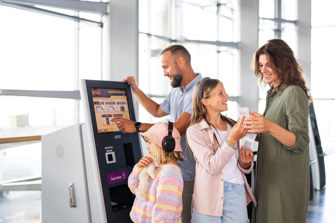 A family with a man, woman, and two children, a slightly older girl and a slightly younger girl, stands by the check-in kiosk at the terminal in Oslo Airport, checking in.