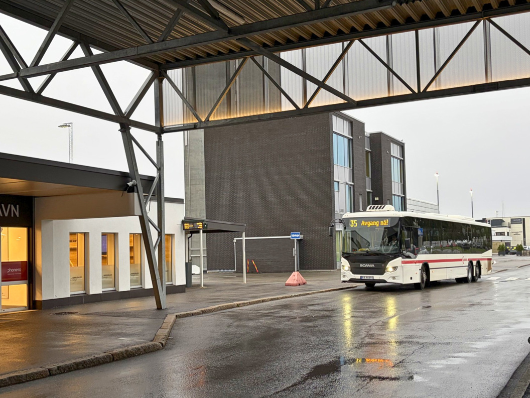 City bus at a modern transit terminal on a wet rainy day, with covered platform and building entrance nearby