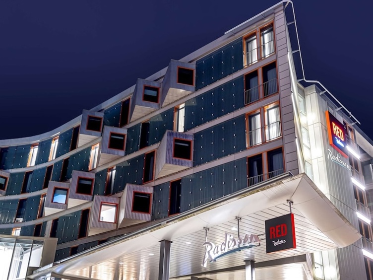Moderne hotellfasade på kveldstid med lys og store vindauge ved Radisson RED hotell