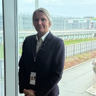 Person in a dress is standing by a large window overlooking an airport, including an air traffic control tower in the background.