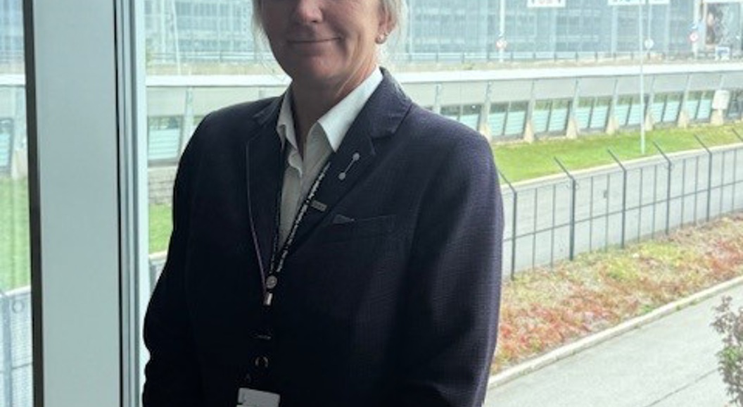 A person in a suit stands by a large window overlooking an airport, including an air traffic control tower in the background.