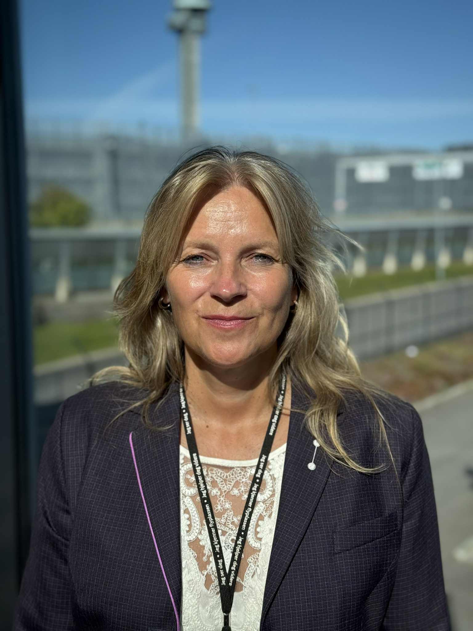 Kvinne i formelt antrekk smiler utendørs med skyfritt vær og bygninger i bakgrunnen.