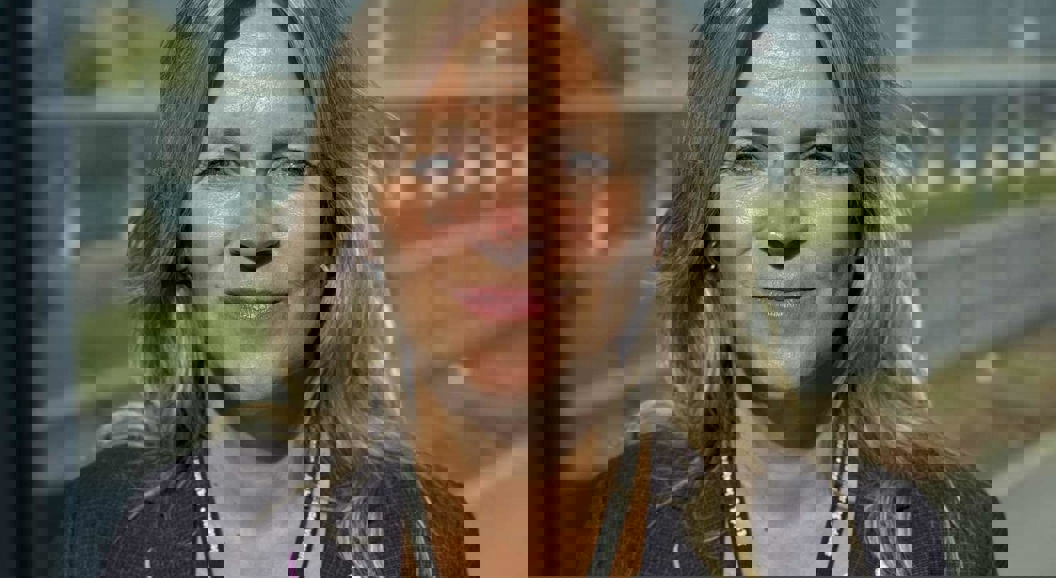 Woman in formal attire smiling outdoors with clear weather and buildings in the background.