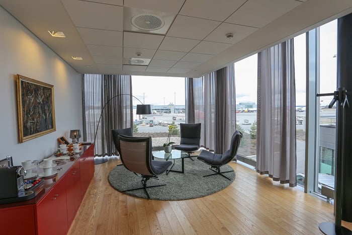 Lyst møterom med utsikt over flyplass, elegant innredet med moderne stoler, et rundt bord og kunst på veggen.