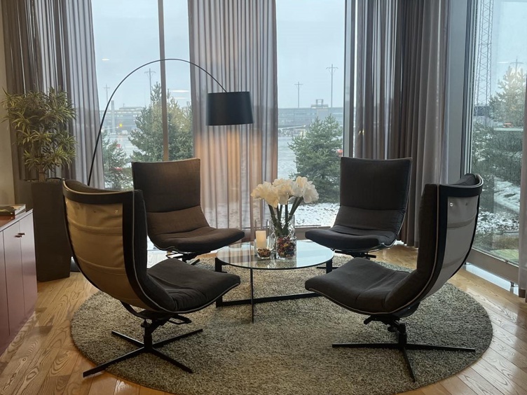 Moderne stue med fire sorte stoler rundt et glassbord, dekorert med hvite blomster, i et rom med store vinduer og utsikt over et vinterlandskap.