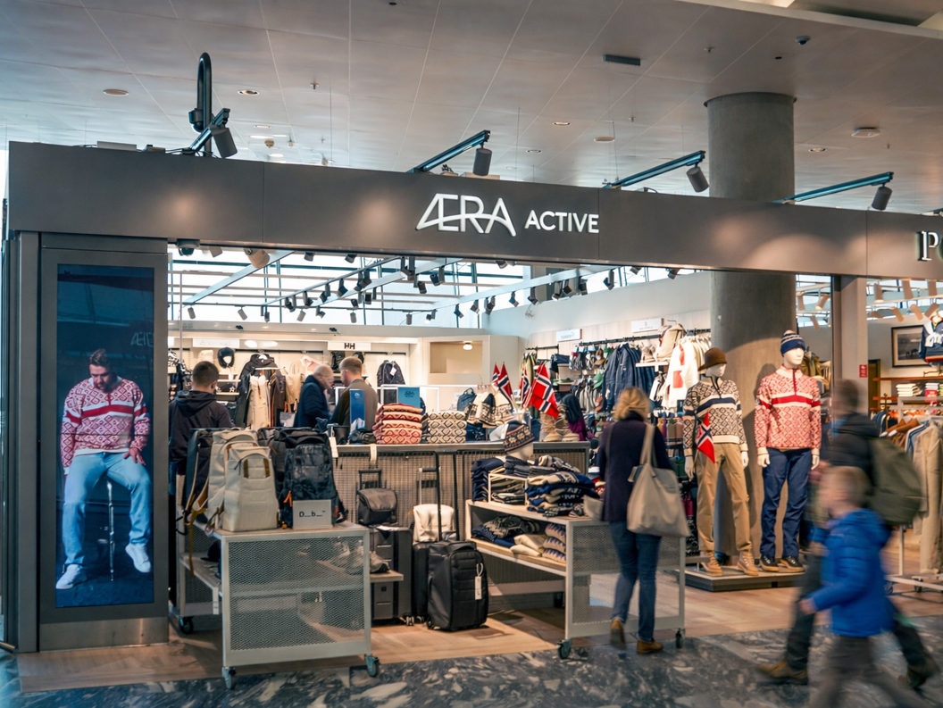 Herreklærbutikkens interiør med pent stablede skjorter, jakker på et stativ, og en mannequin iført en beige blazer, som viser frem en stilfull og organisert butikkvisning