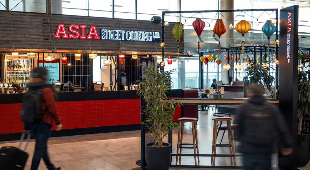 Street art mural featuring an elegant woman in traditional Asian attire holding a bowl of ramen, surrounded by vibrant colors and dynamic brushstrokes. Asian dragon symbol and calligraphy accentuate the composition