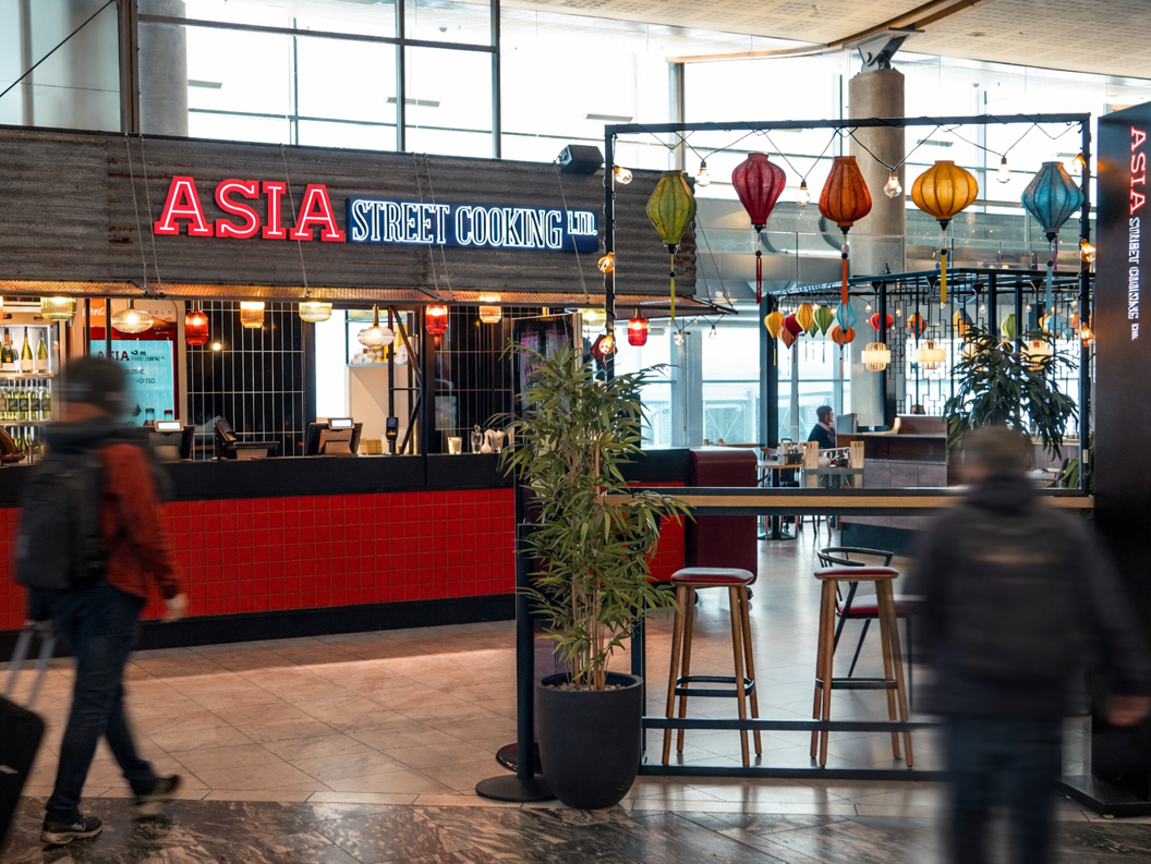 Street art mural featuring an elegant woman in traditional Asian attire holding a bowl of ramen, surrounded by vibrant colors and dynamic brushstrokes. Asian dragon symbol and calligraphy accentuate the composition