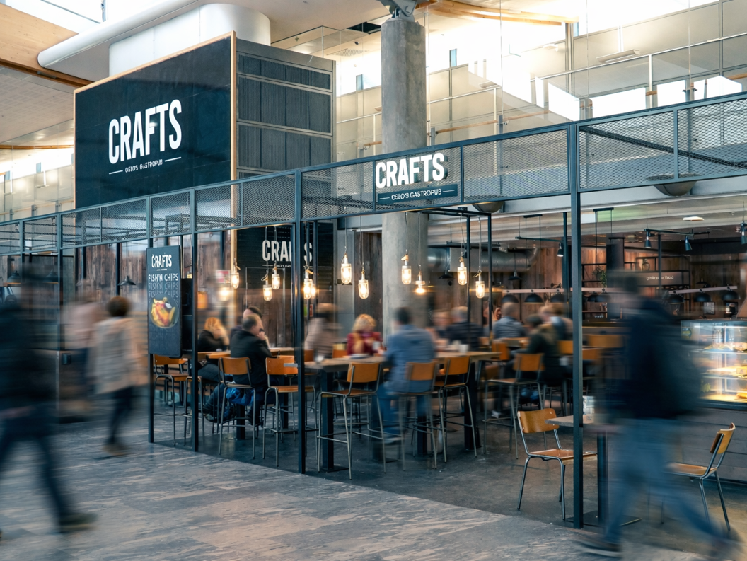 Gourmetburger og søtpotetfries med et glass øl på et bord i en flyplasslounge, fly synlig i bakgrunnen