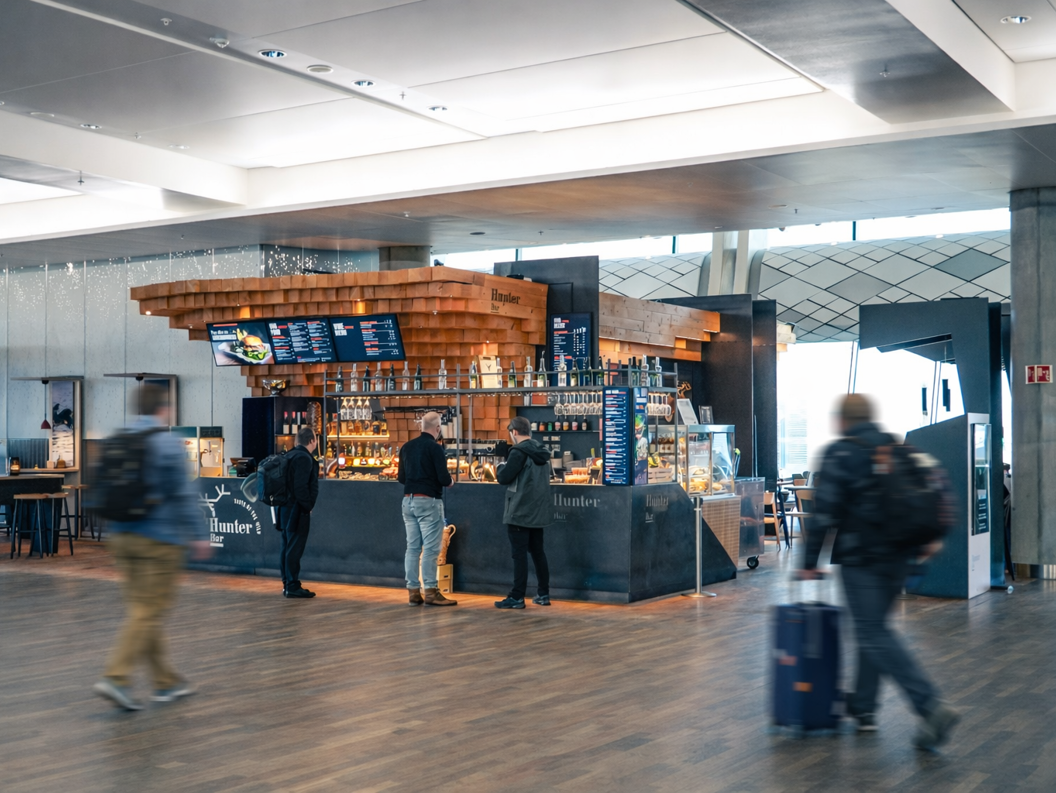 Modern bar interior with wood accents and sleek design at Hunter Bar, showcasing a digital menu, hanging glasses, and a display case with food items