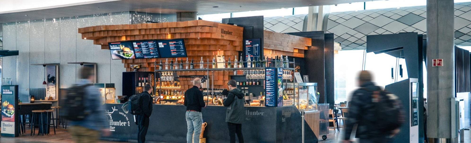 Modern bar interior with wood accents and sleek design at Hunter Bar, showcasing a digital menu, hanging glasses, and a display case with food items