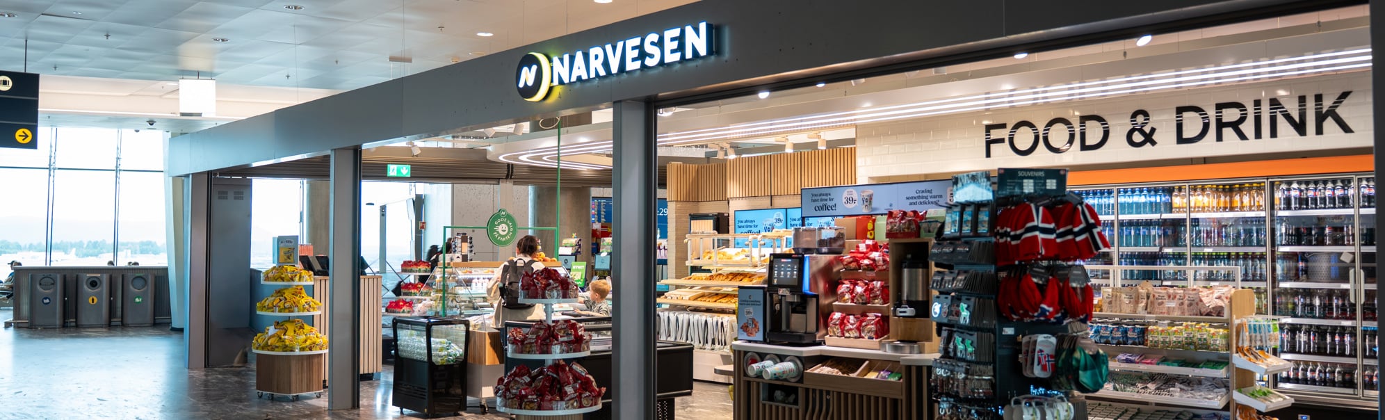 Moderne Narvesen-kiosk på en flyplass som tilbyr nødvendighetsartikler, snacks og drikkevarer under levende belysning