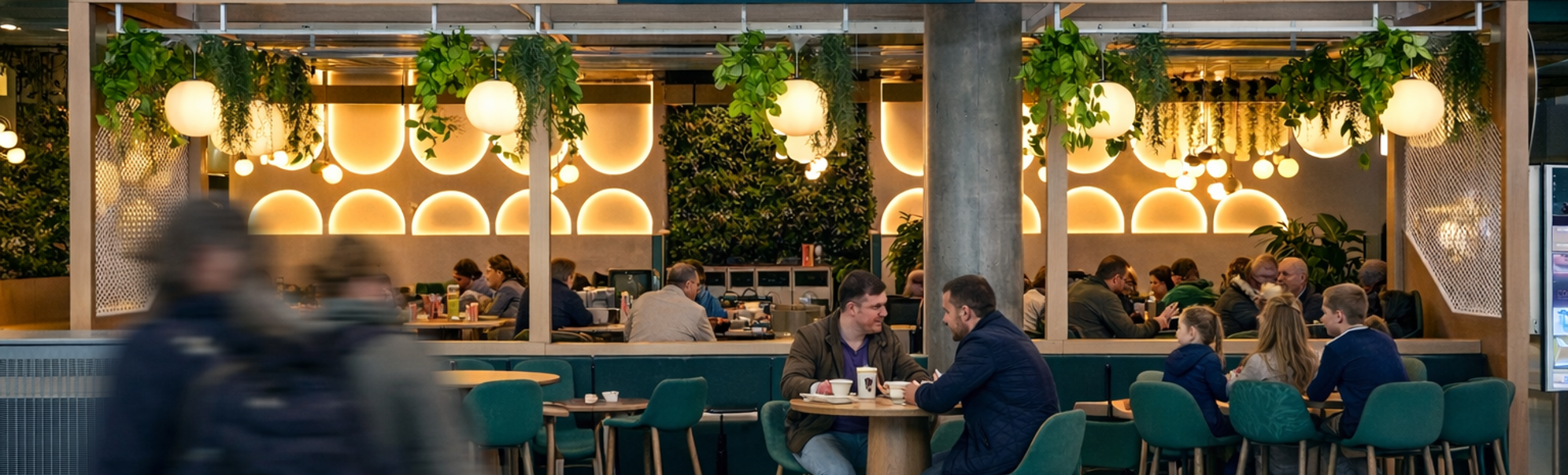 Modern café and dining area with stylish seating, greenery, and ambient lighting, featuring sections for coffee and breakfast, as well as lunch and dinner