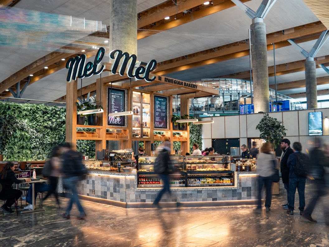 Bakeriutsal ved Mel med nysteikte bakverk og fersk kaffi, moderne interiør og kundar som handlar i lyse, opne lokale