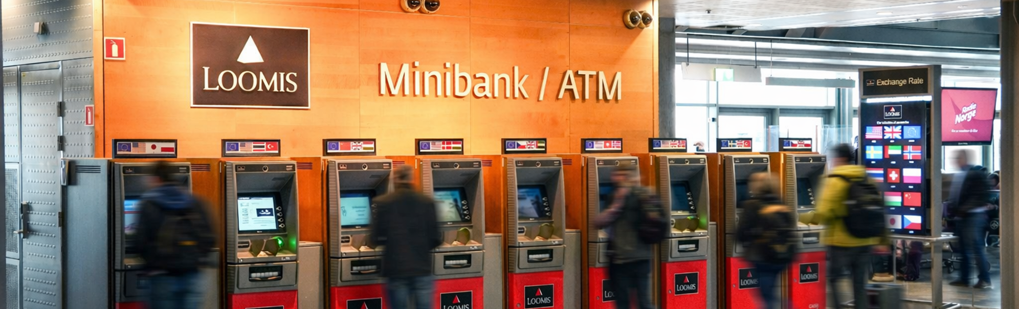 A person using a foreign currency ATM at an airport, with multiple currency options displayed on a screen nearby, indicating international travel and financial transactions