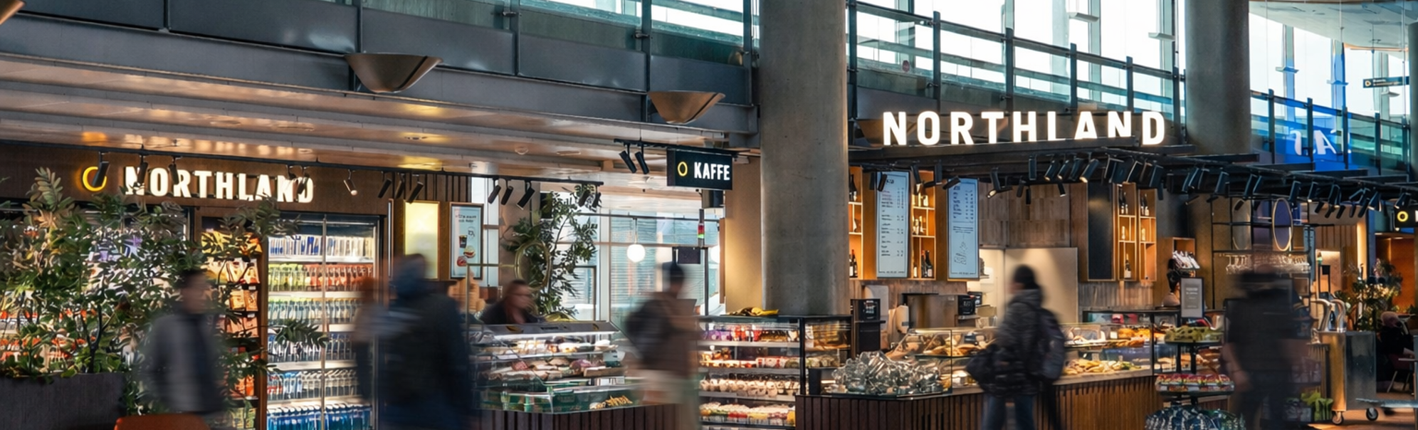 People browsing food selections at a modern airport deli counter with various packaged goods and fresh items