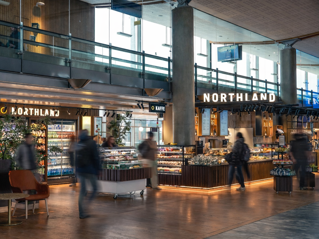 Personar handlar på ein moderne matvarebutikk med ferske produkt i glassdisk. Lyse treoverflater og skilt med terminalnummer i bakgrunnen