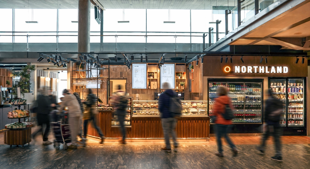 Modern airport convenience store with customers browsing drinks and snacks at Northland, featuring bright interior and a variety of food and beverages on display