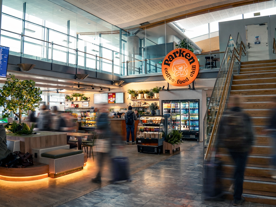 Interiør i en flyplasskafé med et skilt som reklamerer for spaghetti bolognese for 115 valutaenheter; kaféen heter Parken og har en avslappet atmosfære med sitteplasser og planter