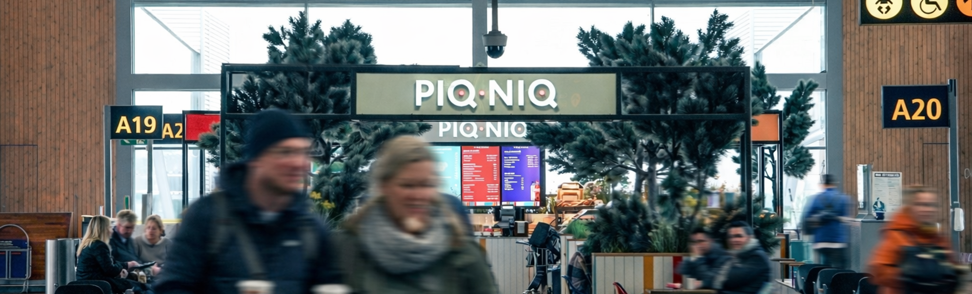 Colorful modern café interior with the sign "PIQNIO" and vibrant stools, a close-up of a coffee grinder and cups, fresh pastries and sandwiches, and decorative plants enhancing the inviting atmosphere