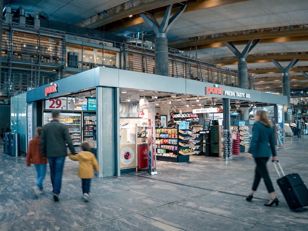 Kiosk i en dagligvarebutikk på en flyplassterminal med snacks, drikkevarer og magasiner utstilt