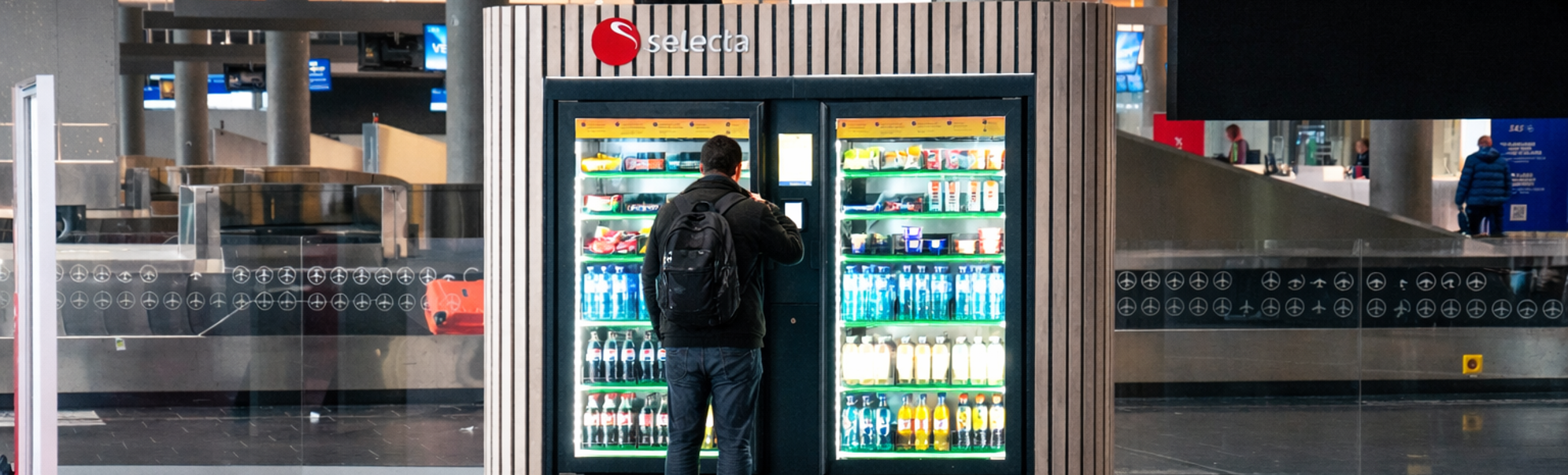 Vending machine filled with assorted snacks and candy bars, including popular brands, with illuminated selection panel