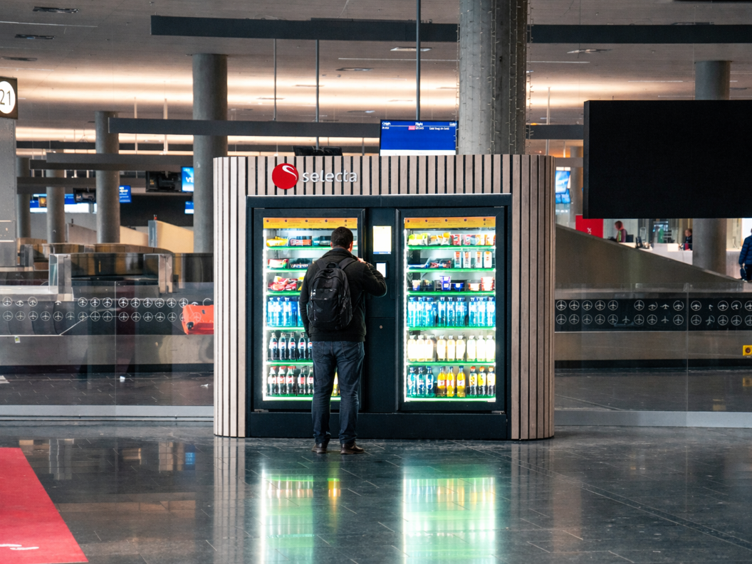 Vending machine filled with assorted snacks and candy bars, including popular brands, with illuminated selection panel