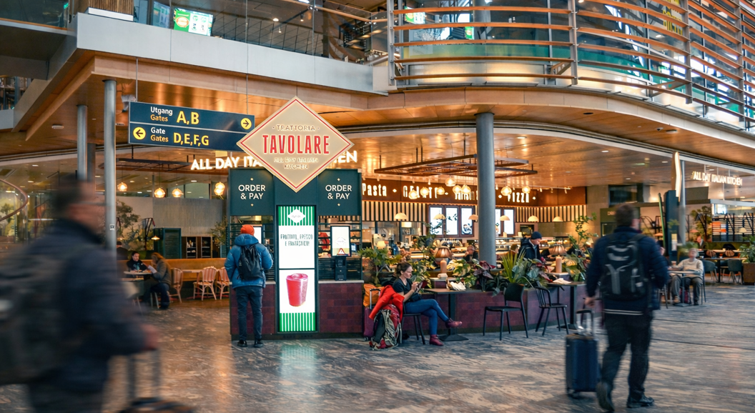Bar staff working behind a modern bar counter, smiling and organizing drinks, with a stylish interior featuring hanging lamps and word art on the walls