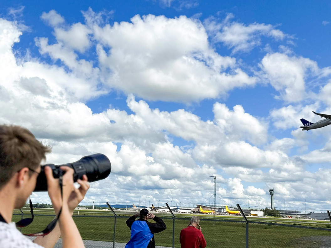 A photographer takes pictures of a passenger plane taking off on a cloudy day at an airport.