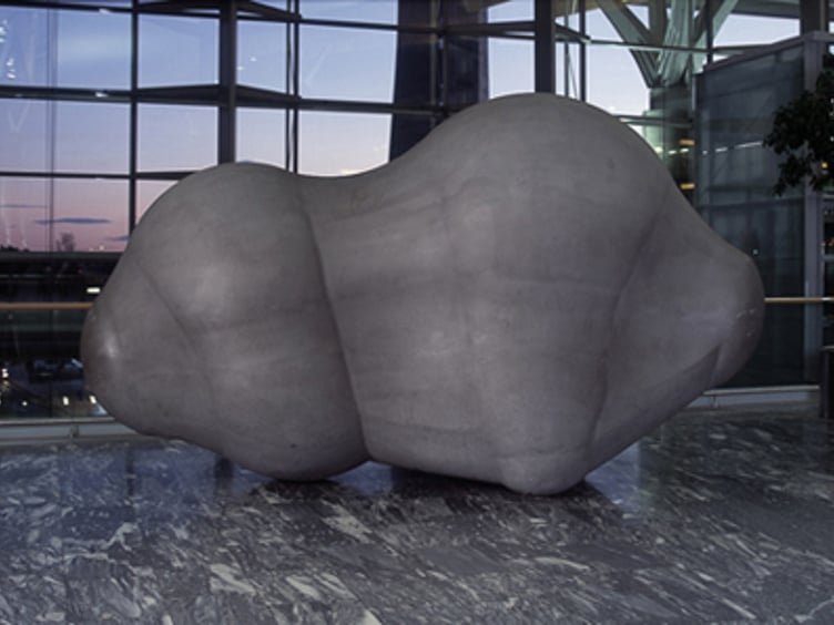 Skulptur av en abstrakt, organisk formet stein, plassert i en moderne bygning med store vinduer og marmorgulv