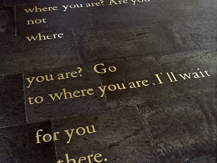 Tekst inngravert i gulvfliser, som stiller spørsmål om personlig tilstedeværelse og lover å vente der man befinner seg
