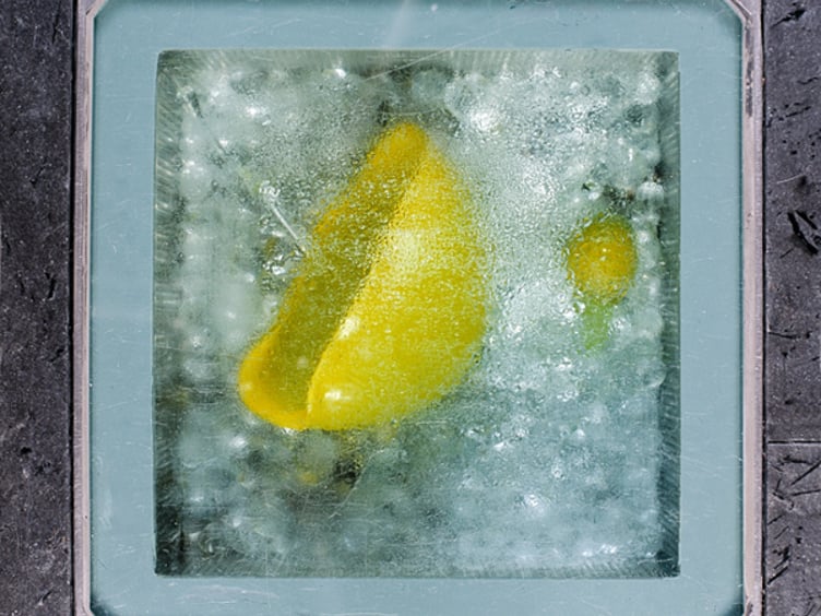 Gult eplefruktstykke frosset i is, sett fra oven med en grå ramme rundt
