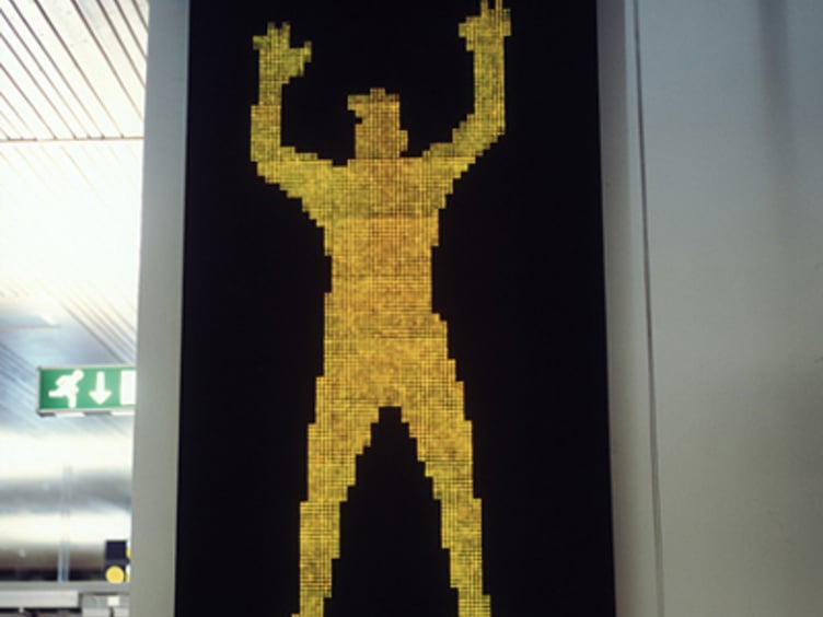 Mosaikkunstverk med gul silhuett av menneskefigur mot svart bakgrunn, hengt på vegg i offentlig bygning