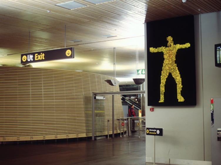 Skilt ved flyplass med teksten "Ut Exit" og en lysende gul figur ved siden av