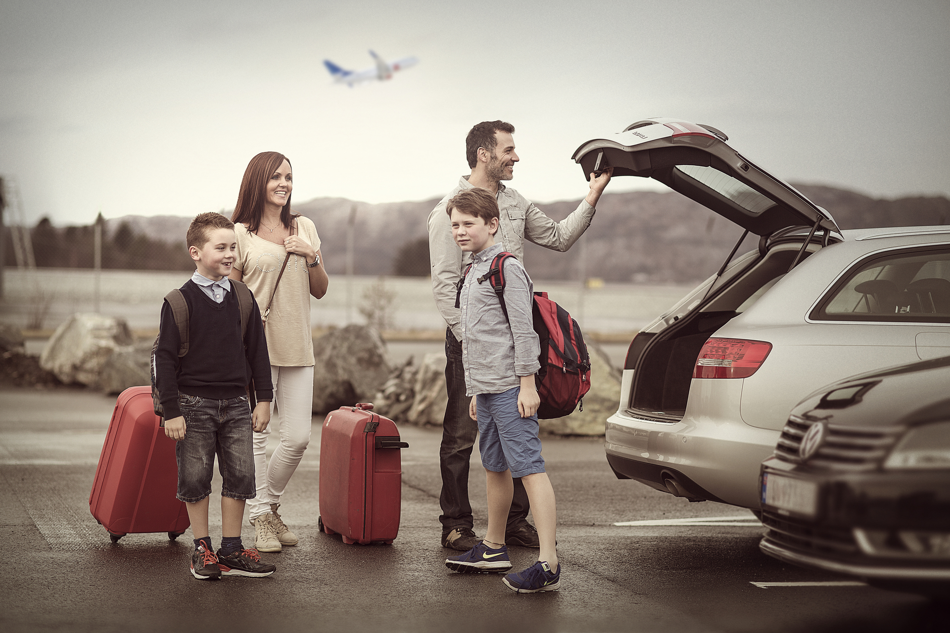 Family at the parking lot with luggage and car, ready for travel. Airplane in the background.