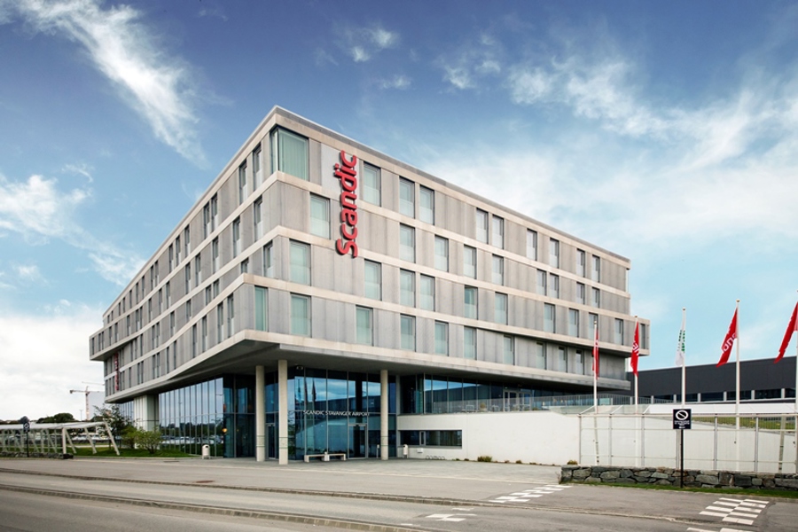 Modern Scandic hotel facade near Stavanger Airport, surrounded by blue sky and flags.