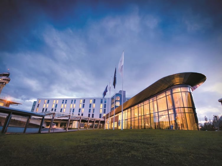Modern hotel building with glass facade next to airport tower at dusk, surrounded by green grass.
