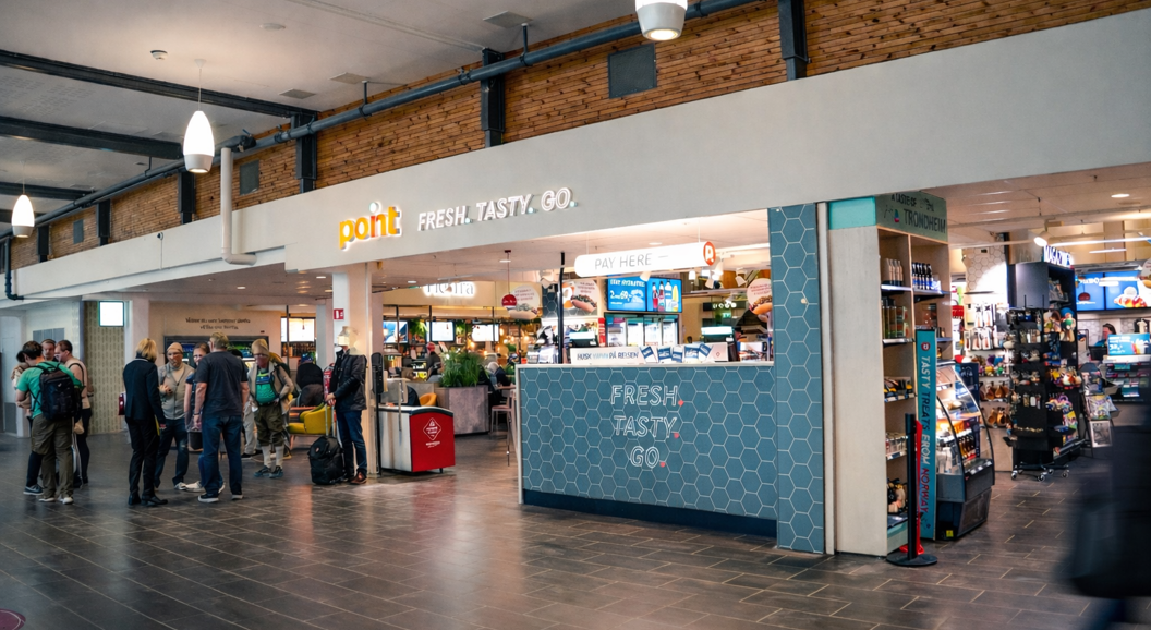 Person som holder en bunke med magasiner og bøker, med et synlig "Stella" magasin på toppen, med en uskarp bakgrunn i en bokhandel