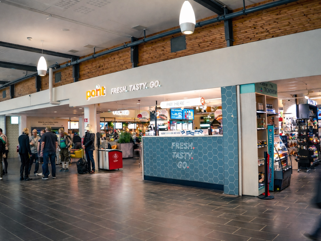 Person som holder en bunke med magasiner og bøker, med et synlig "Stella" magasin på toppen, med en uskarp bakgrunn i en bokhandel