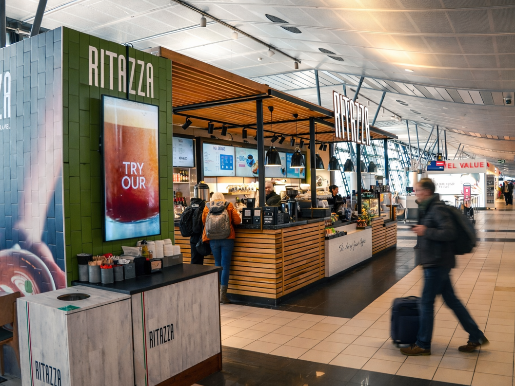 Kunder som venter ved disken i kaffebaren Caffè Ritazza, med en variert meny og Lavazza-merkevare, plassert i en flyplassterminal