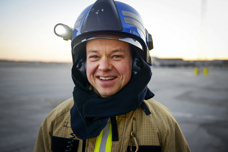 Firefighter in uniform and helmet smiling outdoors at sunset.