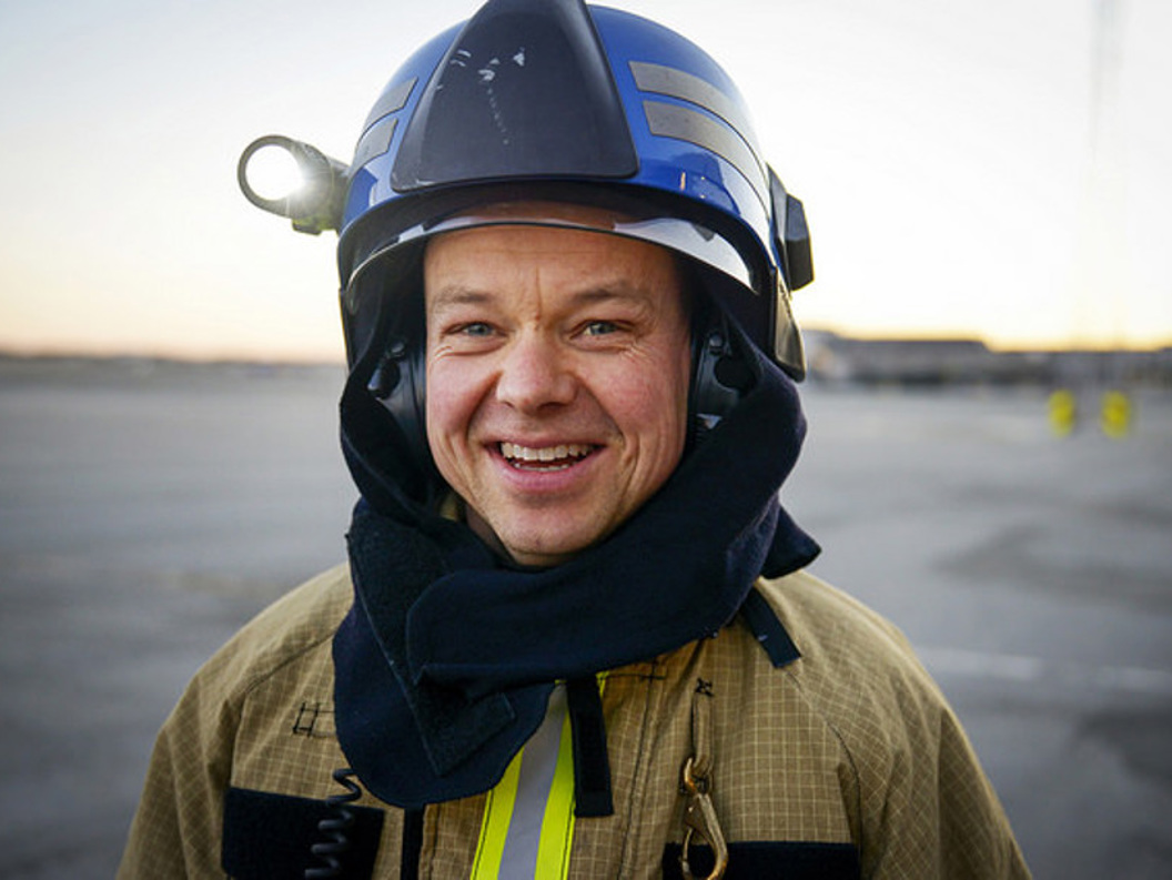 Firefighter in uniform and helmet smiling outdoors at sunset.