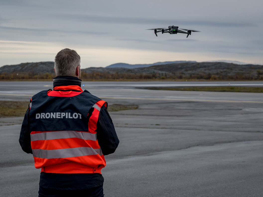 Man in orange jacket with drone pilot vest flying drone at an airport