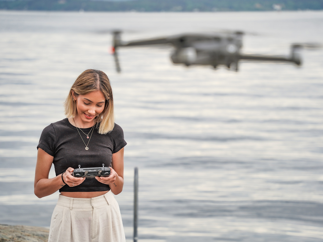 Woman smiling while flying a drone by the sea and looking down at the controller