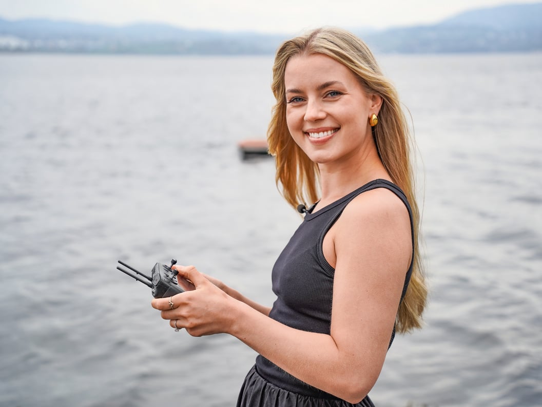 Woman looking at the camera and smiling while flying a drone by the sea